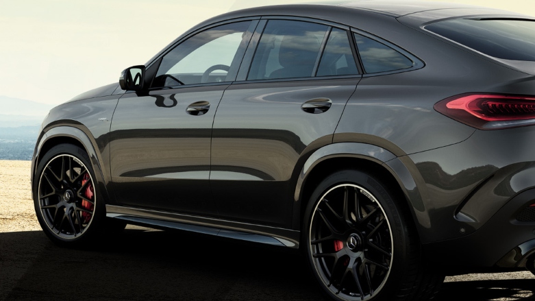 Vista trasera de SUV Mercedes-AMG GLE Coupé color gris sobre terreno rocoso con fondo de atardecer. 