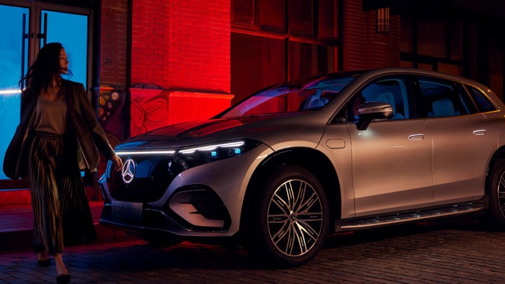 <p>Vista lateral delantera de Camioneta Eléctrica Mercedes-Benz EQS SUV color gris estacionada en la calle con una mujer al frente caminando.</p>