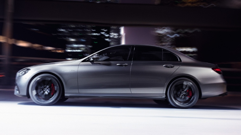 Vista lateral de carro deportivo de lujo Mercedes-AMG Clase E color gris siendo conducido por calles de la ciudad.